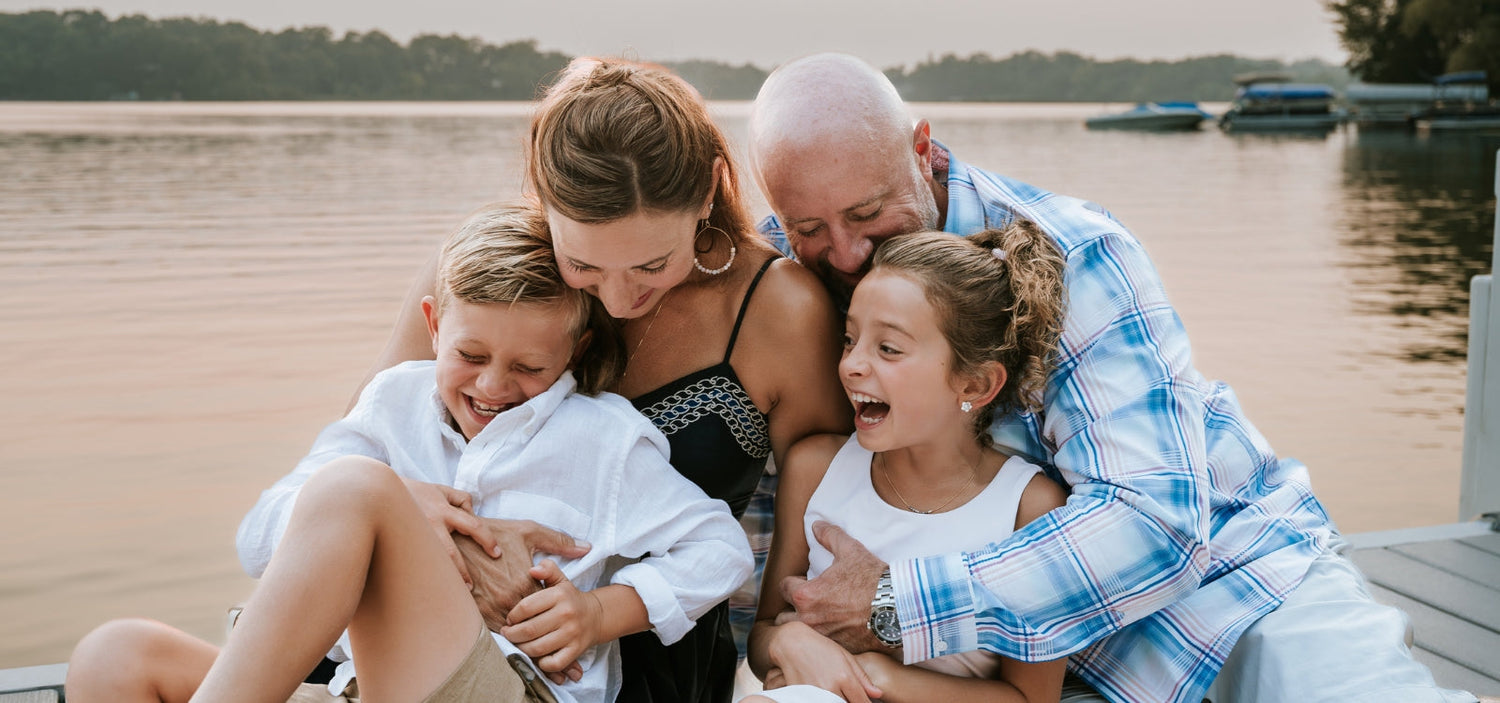 Woman and family sitting together on a dock by a peaceful lake, representing healthy aging, wellness, and long-term lifestyle habits that support women’s longevity.
