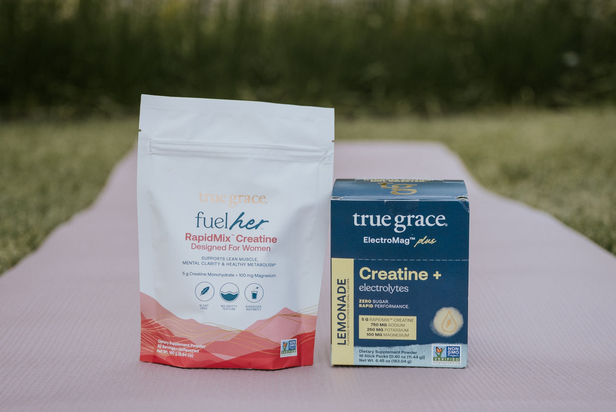 FuelHer™ RapidMix™ Creatine pouch and ElectroMag® Plus Creatine Lemonade carton on a pink yoga mat in a garden
