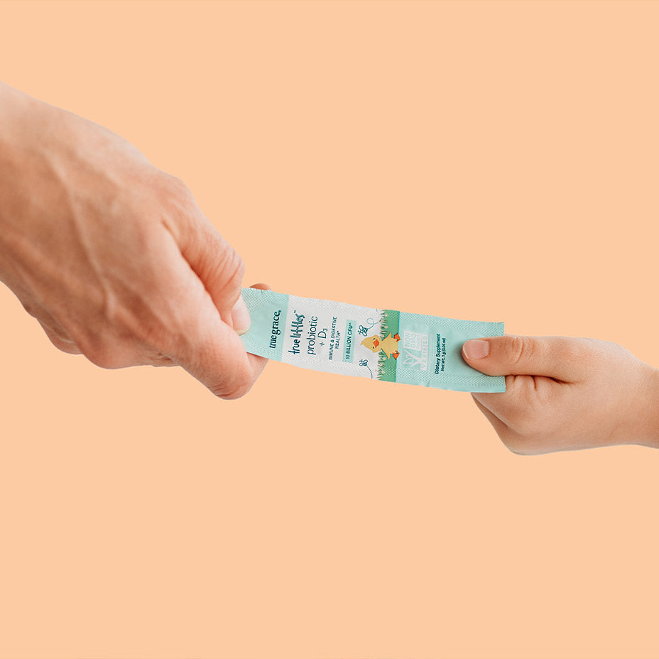 One hand passing True Littles probiotics to a smaller hand