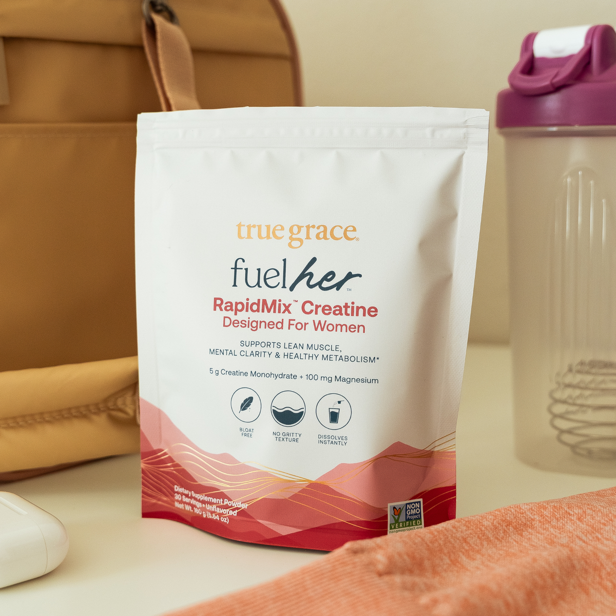A stand-up pouch of true grace fuel her RapidMix Creatine powder, placed on a tabletop with a tan bag and a shaker bottle in the background.