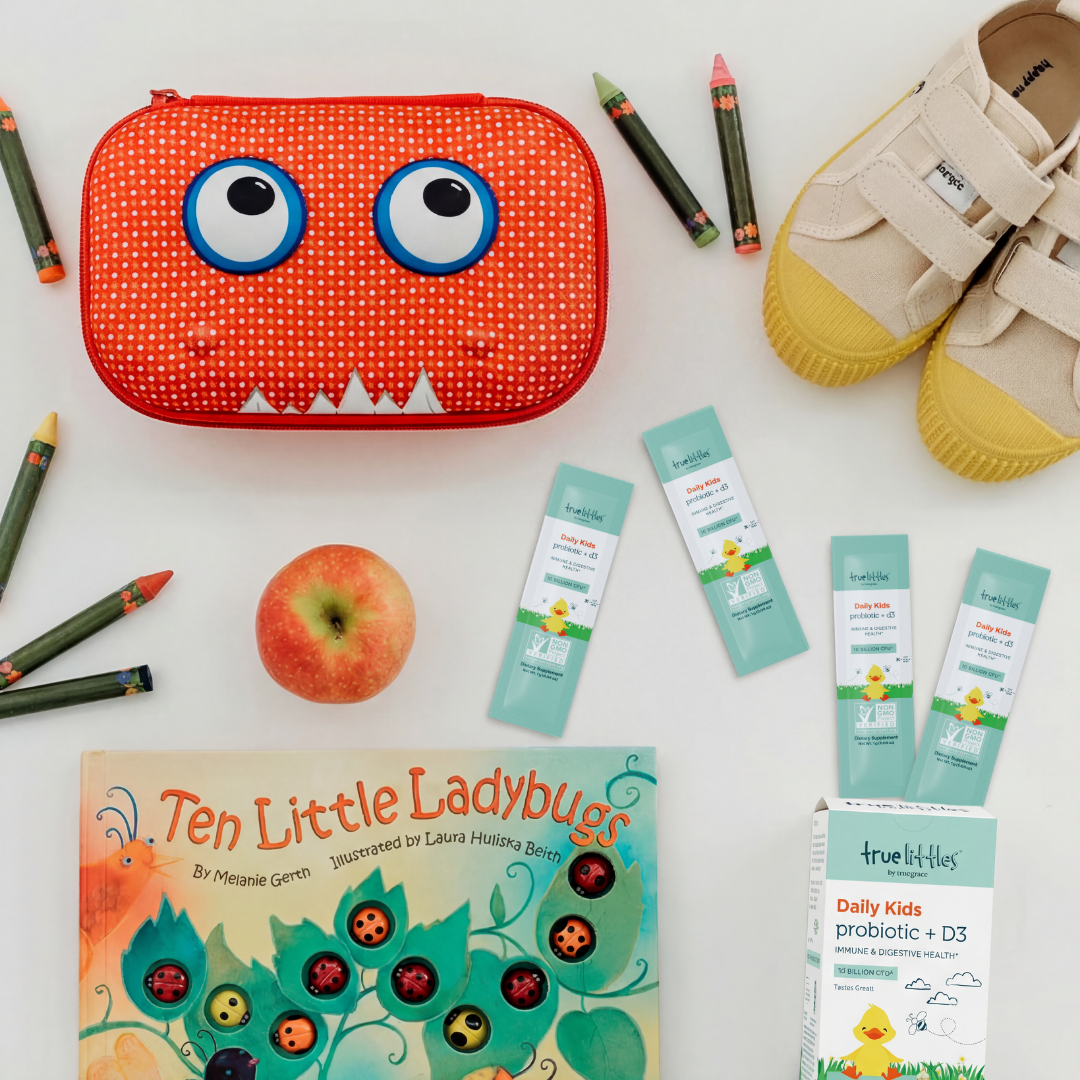 Red monster-shaped pencil case with a book, apple, and baby shoes on a white background