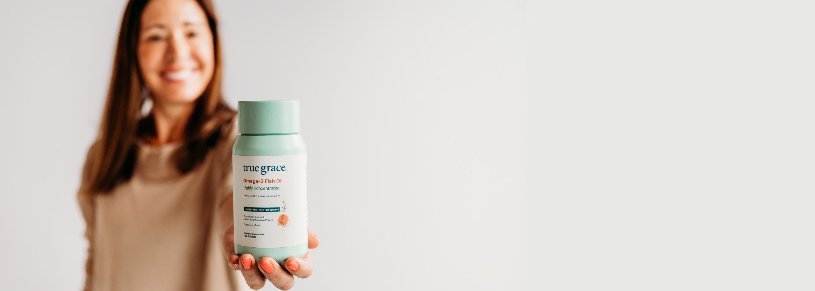 Woman holding a bottle of True Grace Omega-3 Fish Oil supplement with a white background