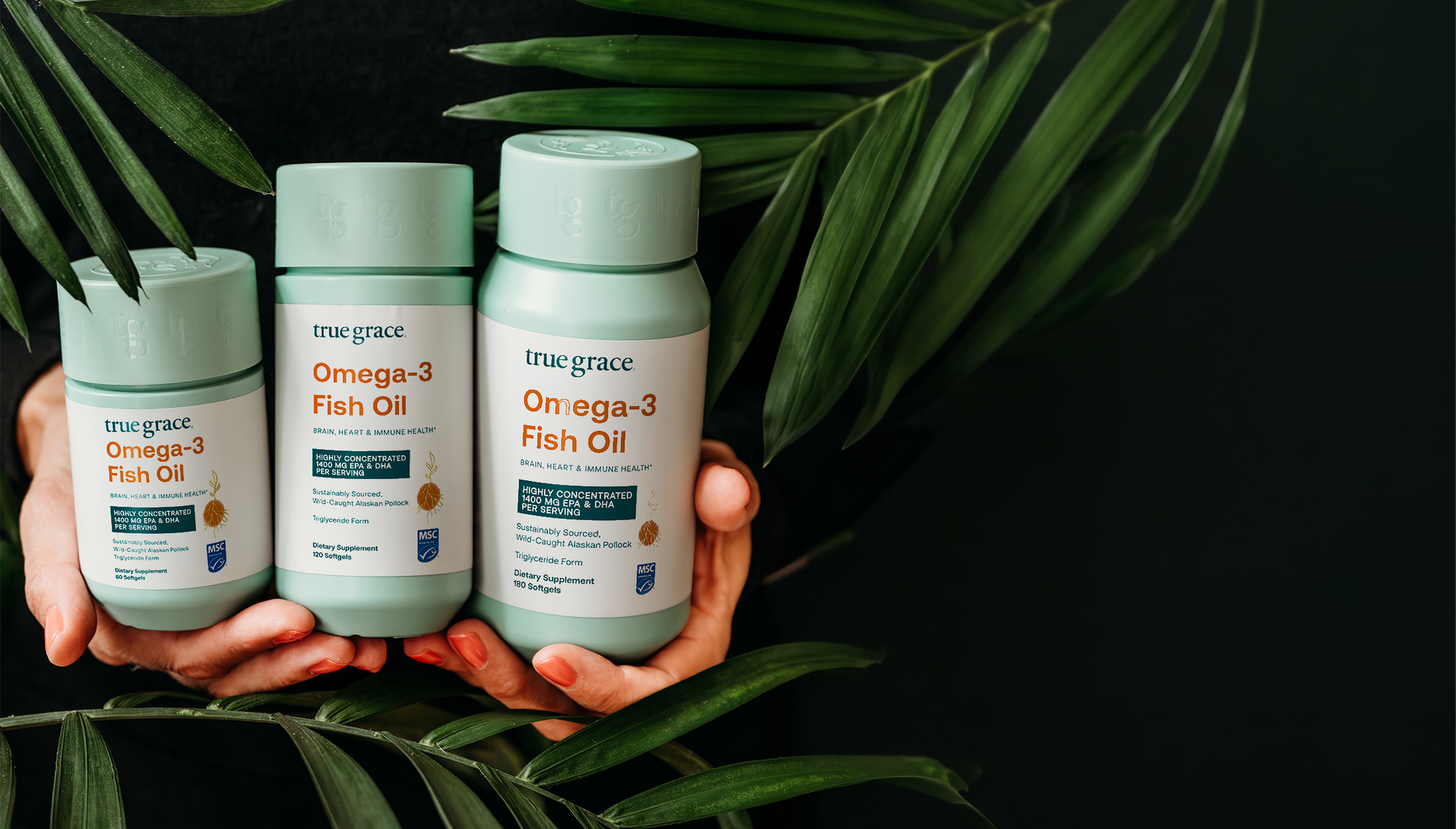 Three bottles of true grace Omega-3 Fish Oil held between hands with green leaves in the background