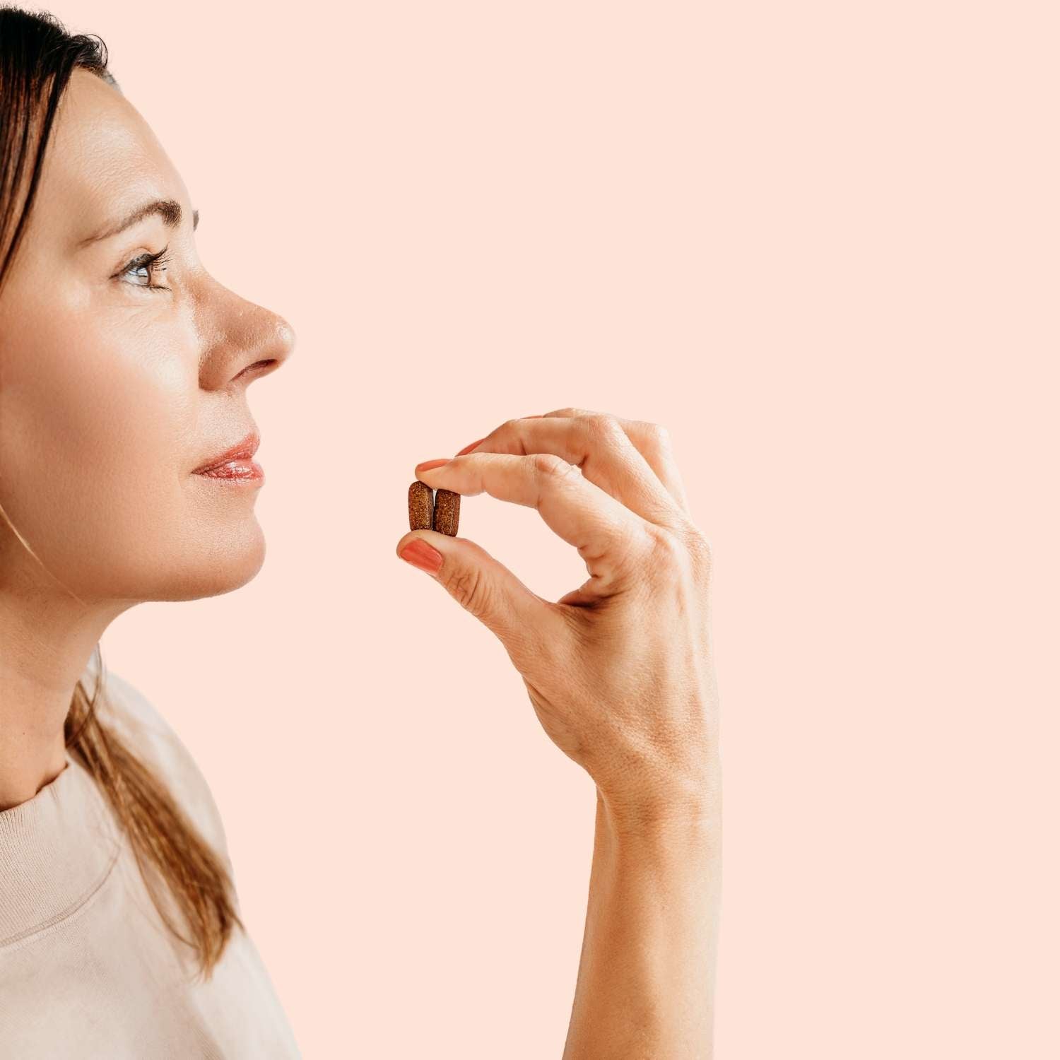 Woman holding a small pill in a pink background