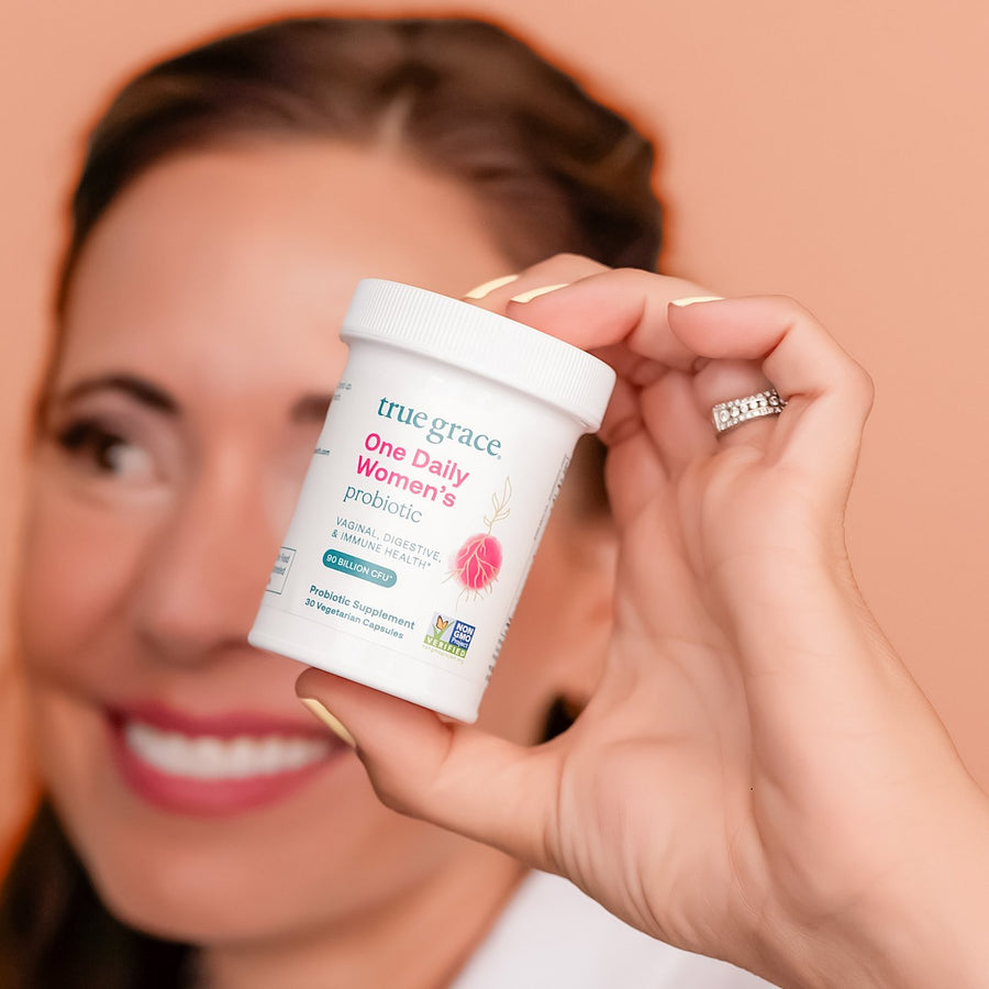 A smiling woman holding up a bottle of One Daily Women's Probiotic