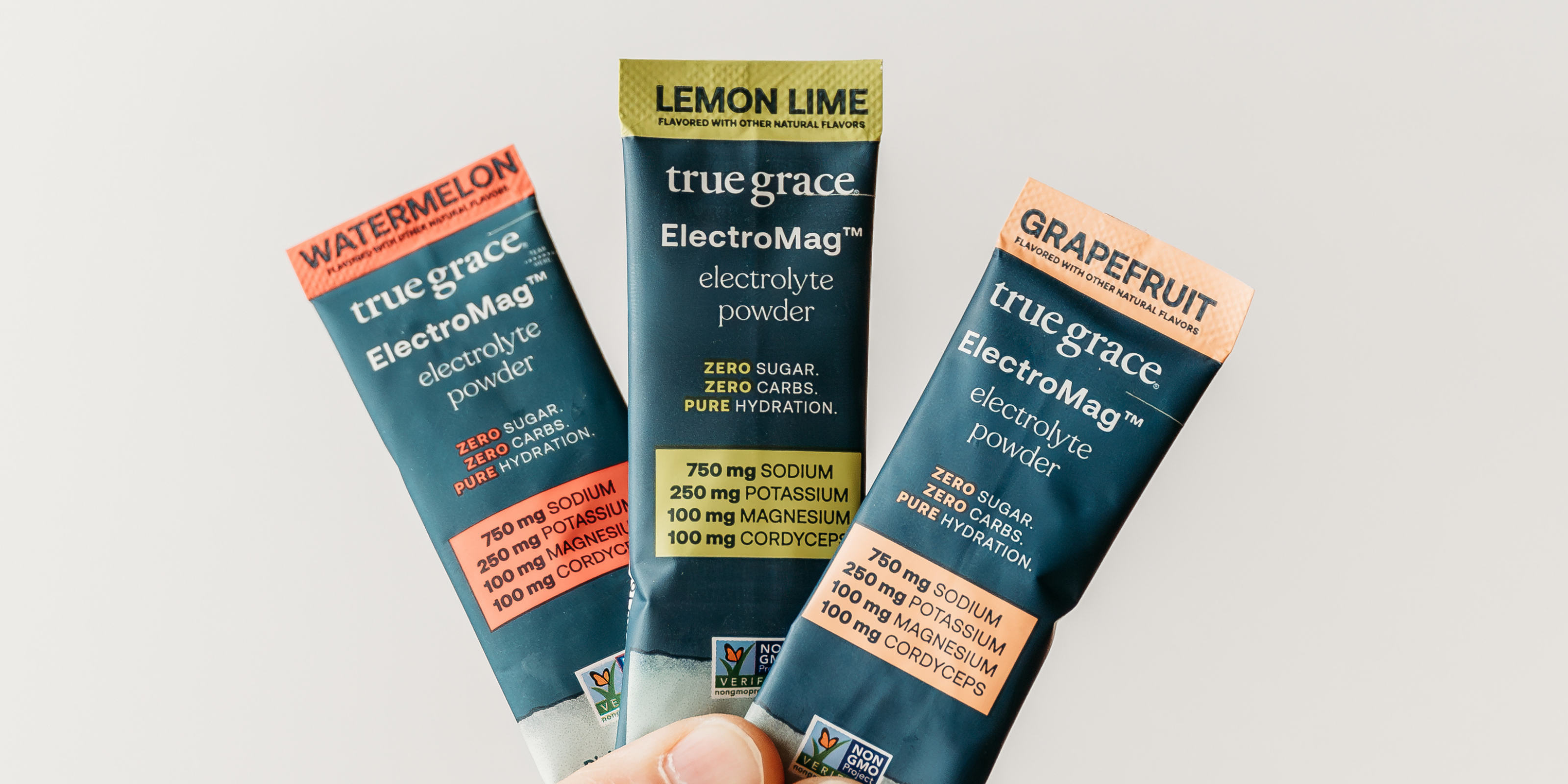 Three packages of true grace ElectroMag electrolyte powder in different flavors on a light gray background.