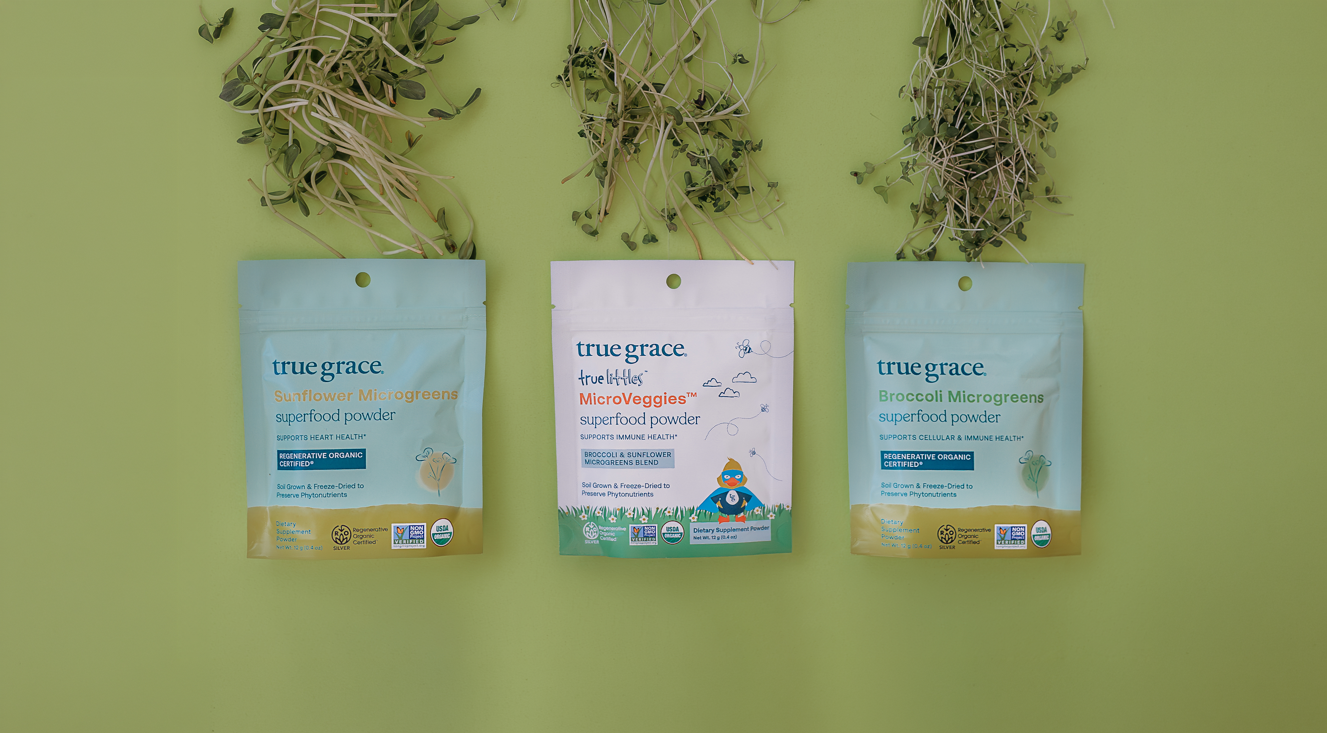 Three packages of True Grace superfood microgreens and microveggies powder on a green background