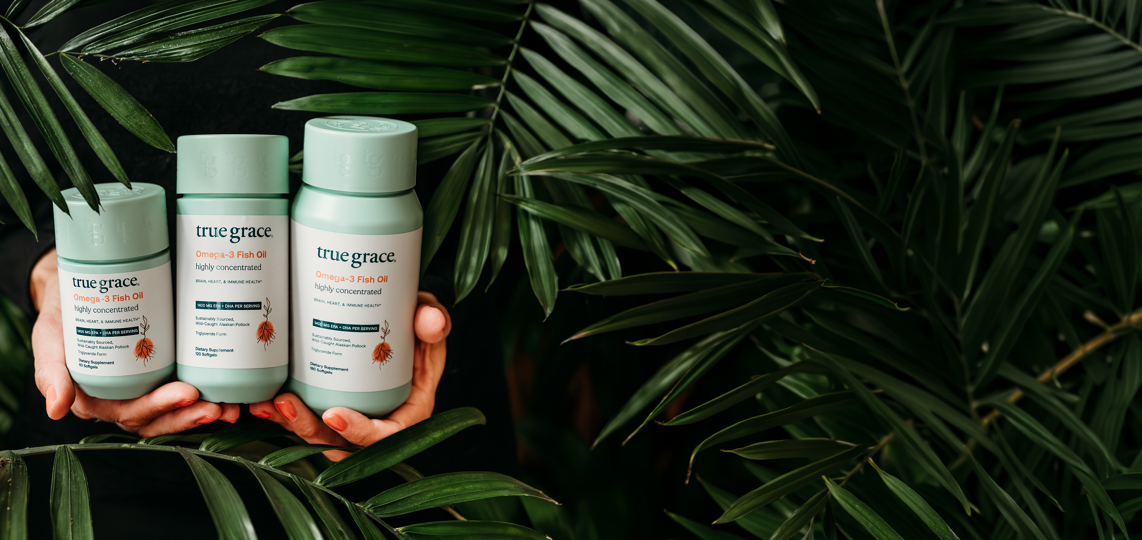 Three True Grace Omega-3 Fish Oil bottles held against a leafy green background