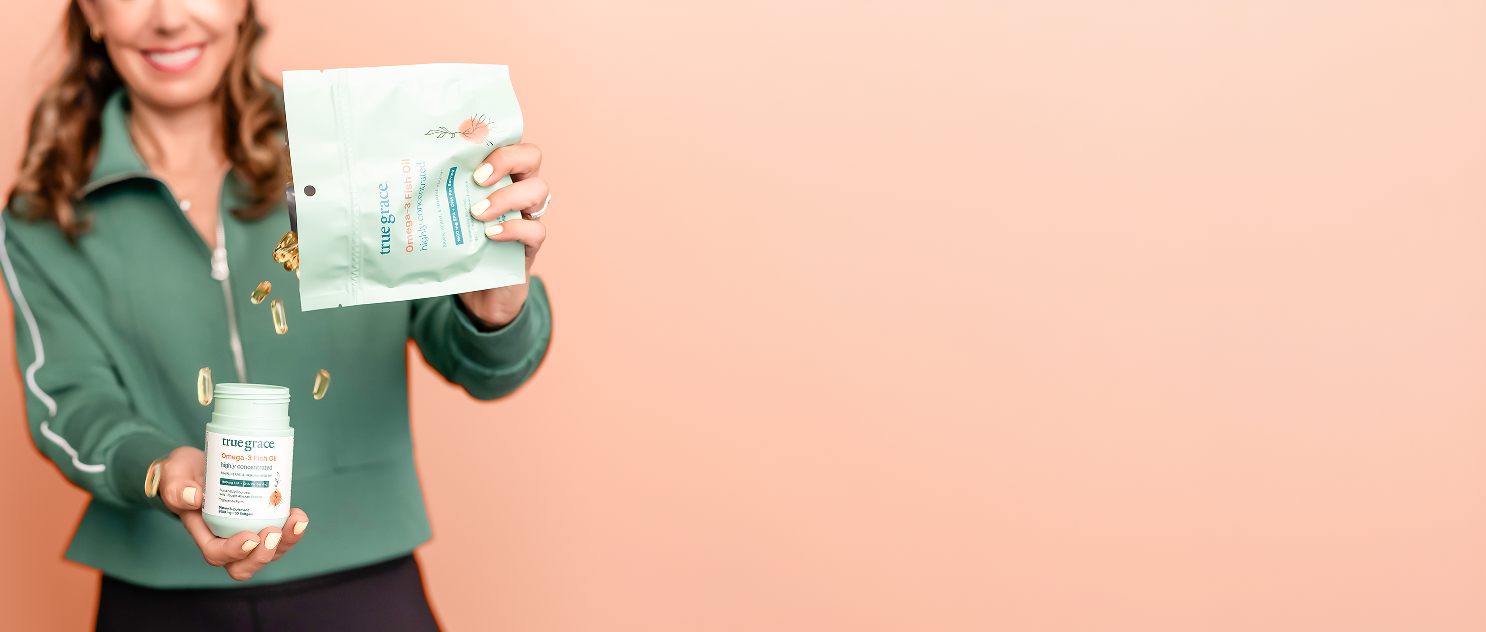 Person holding two containers of True Grace Omega-3 Fish Oil packages with a plain background
