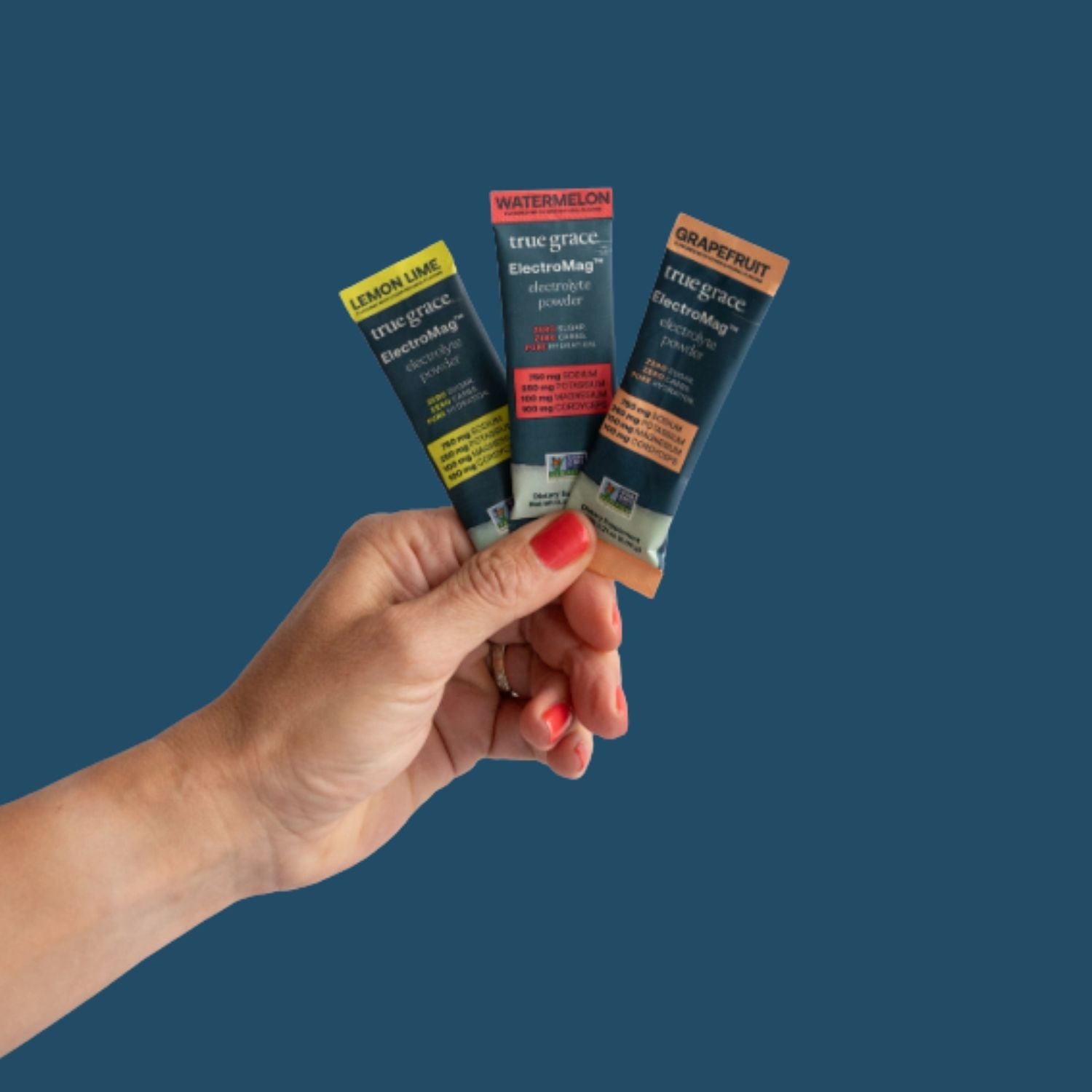 Hand holding three small packages of  electrolyte powder of different flavors against a blue background